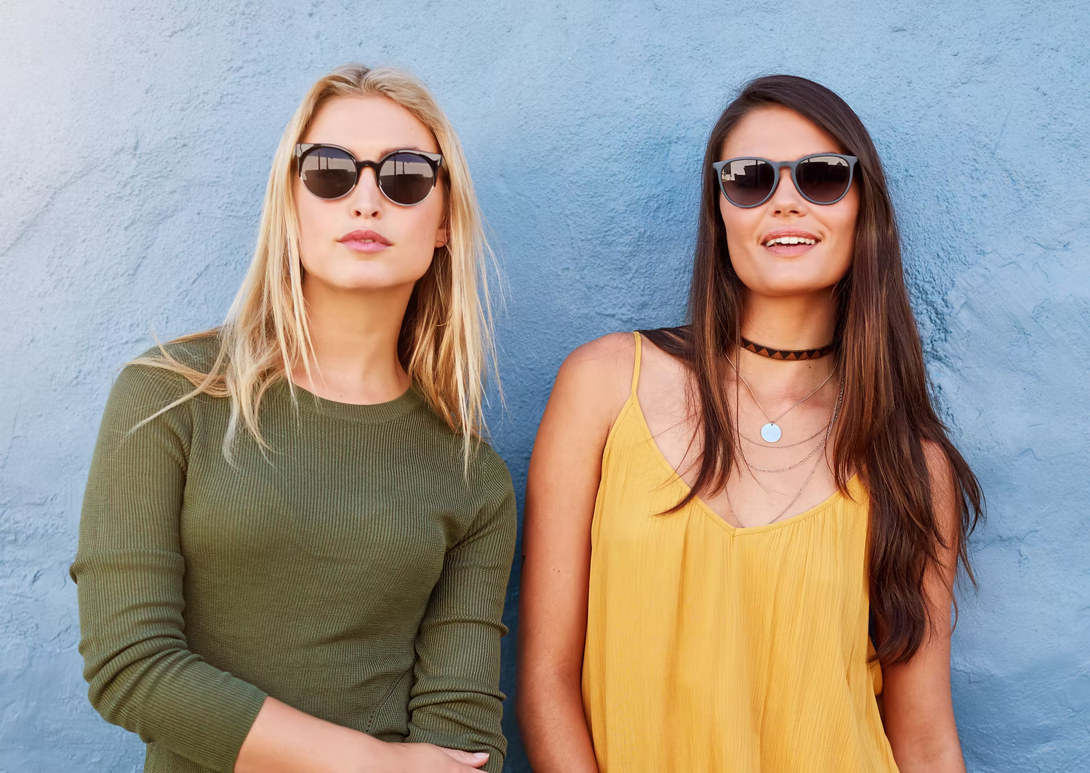Zwei Frauen mit Sonnenbrillen vor einer blauen Wand